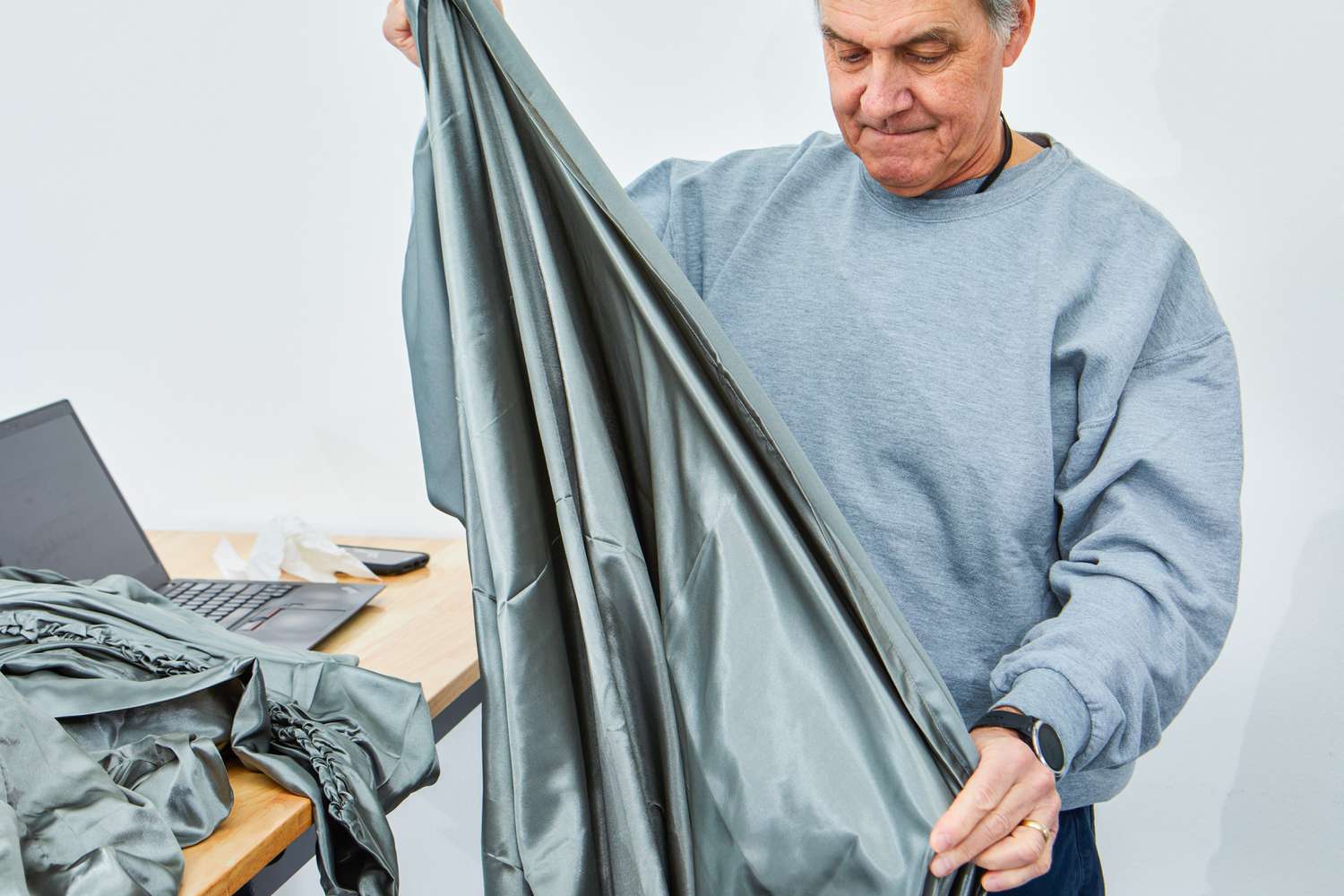 Person holding Person Lanest Housing Silk Satin Sheets next to a table with a laptop 