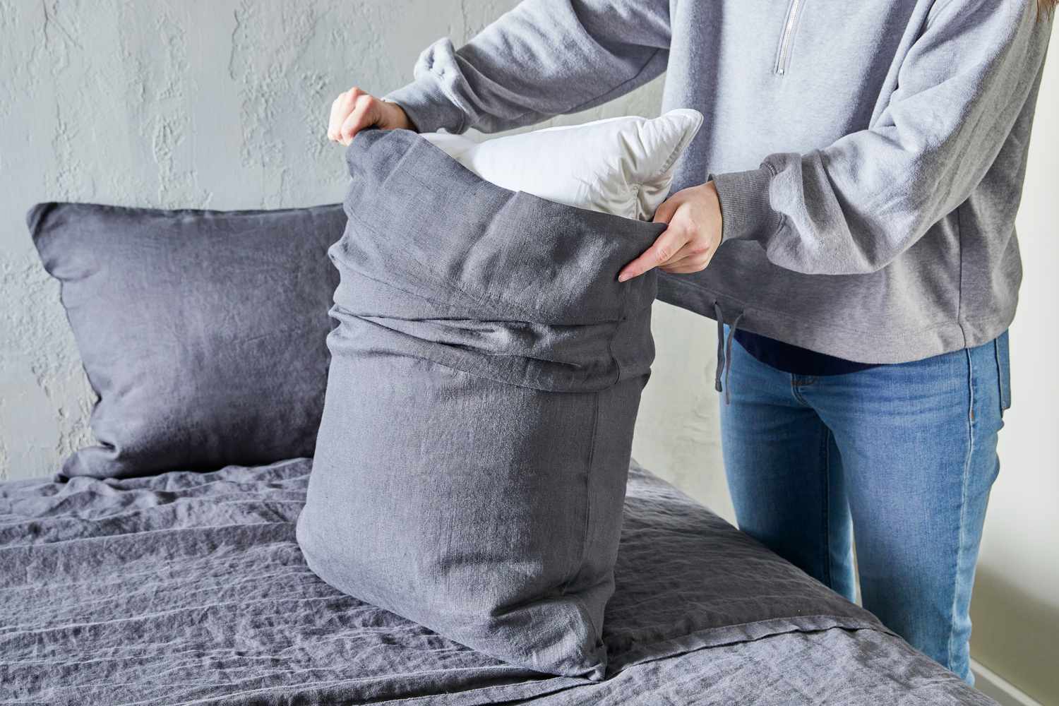 Person putting a pillow in the Quince European Linen pillow cover on a bed 